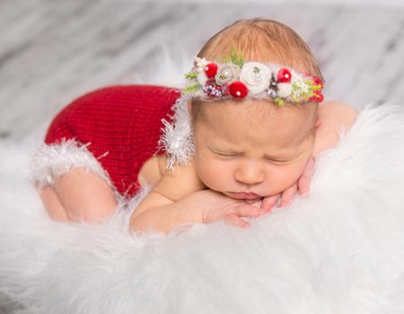 lovely newborn girl in red romper and colorful headband sleeping on white fluffy blanket