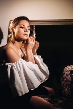 Beautiful girl in the mirror reflection at home. Girl before the holiday near the home mirror.A girl in a white dress with long hair is going to a party at home.