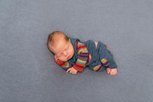 Sweet hairy newborn napping on his side, in striped pants and jacket