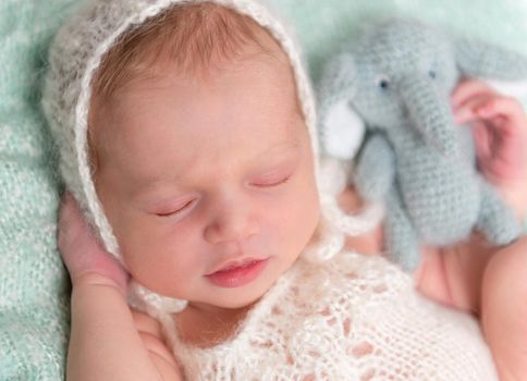 beautiul sleeping newborn baby in hat with toy in hand, closeup