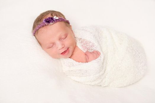 cute newborn baby in headband with flowers smiling asleep, closeup