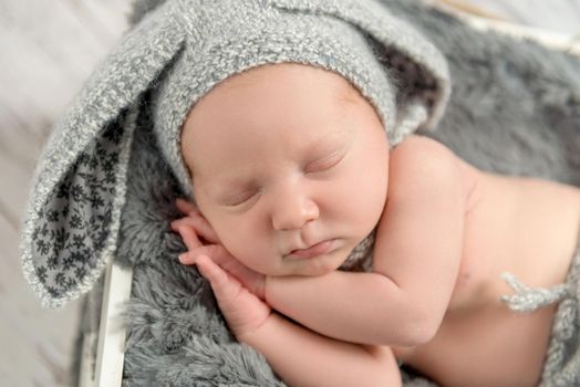 sweet sleeping baby in gray panties and hat with hare ears with toy on basket, top view