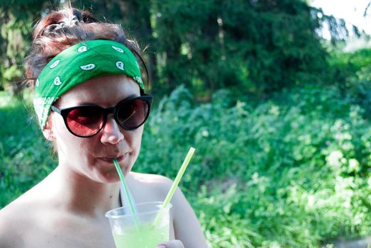 Young beautiful girl drinking a green drink from a plastic cup takeaway food. Summer cold drinks.