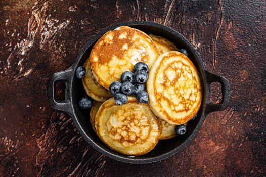 Fried Pancakes with fresh blueberries and maple syrup in a pan. Dark background. Top View.