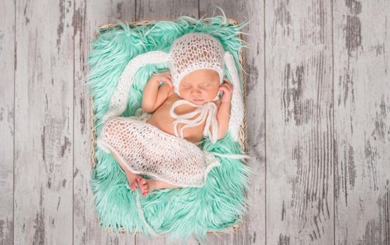 funny sleeping newborn in panties and hat on a cot with turquoise blanket, top view