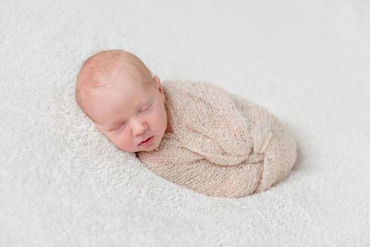 lovely sleeping baby wrapped in beige diaper on white blanket