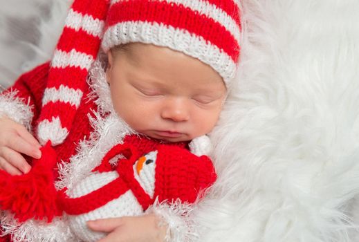 Newborn dressed in a costume, holding a snowman knitted toy in his sleep, closeup