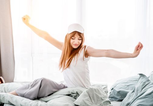 Pretty girl wakes up in the room with sunlight, smiling and stretch her body in the bed. Young beautiful woman wearing pajama in the morning time in the bedroom. Concept of good rest
