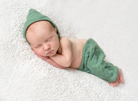cute newborn sleeping in green elf hat and panties on soft white blanket