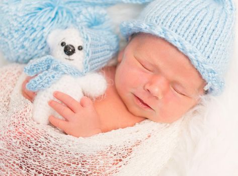 Slightly frowning adorable baby sleeping with his teddy bear, closeup