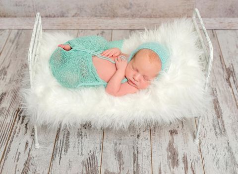 lovely wrapped newborn sleeping on cot with white soft blanket and toy