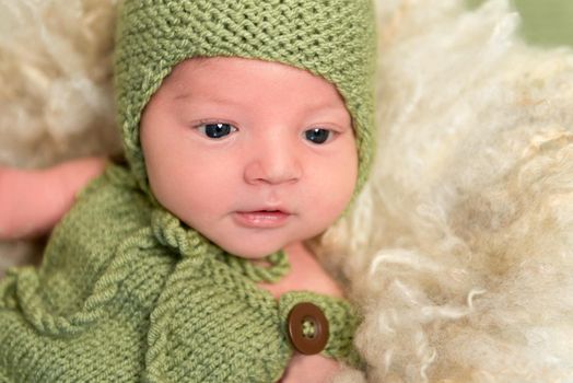 Adorable baby in a knitted green outfit, with his eyes wide opened, resting, closeup