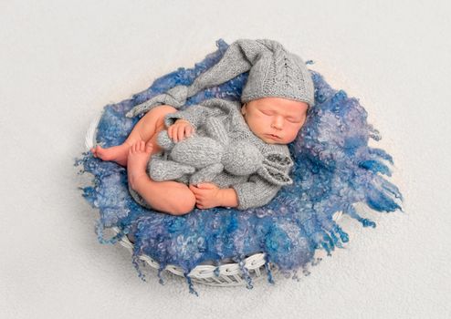 Infant in cute grey knitted outfit sleeping with his favorite toy on a fluffy pillow