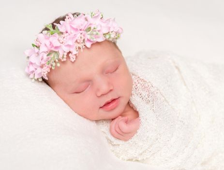 cute newborn baby in headband with flowers smiling asleep, closeup