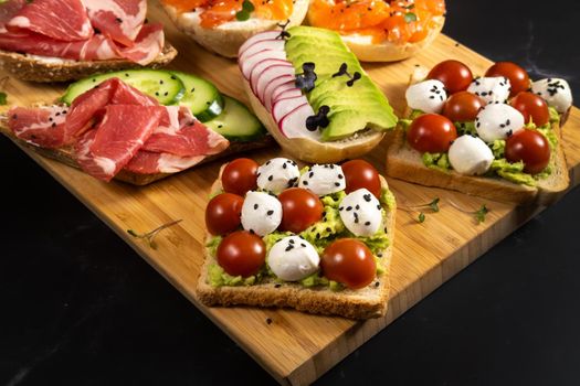 An assortment of sandwiches with fish, cheese, meat and vegetables lay on the board and a bun.