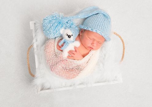 Sleeping kid in enourmous knitted hat holding a teddy, wrapped in a blanket, topview