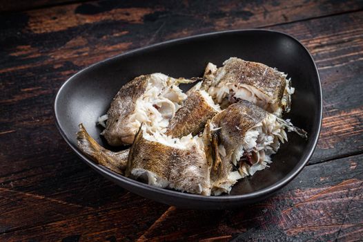 Roasted hake white fish in a plate. Dark wooden background. Top view.