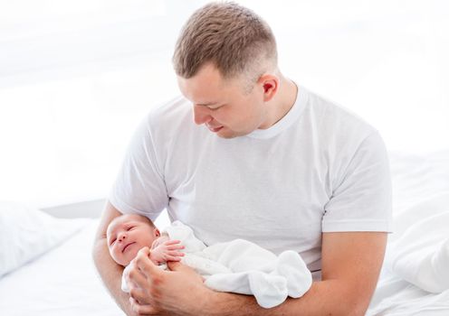 Adorable newborn baby girl wearing white costume sleeping in father hands. Cute infant child napping at home and parent dad holding her