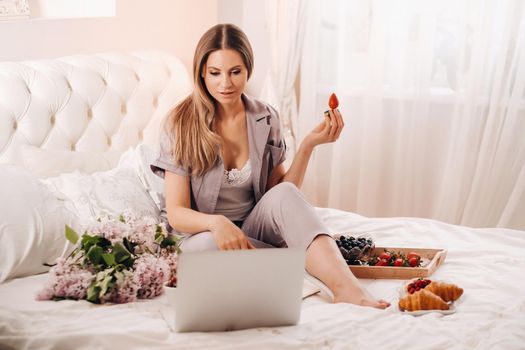 a girl sits in bed in the evening watching a laptop and eating strawberries, a girl in bed eats sweets before going to bed.