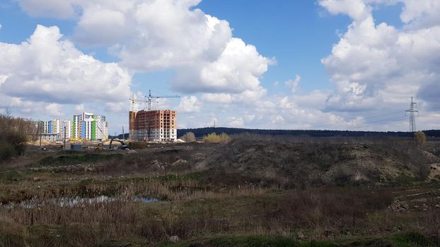 A snapshot of the field and the construction of multi-apartment high-rise residential buildings that began there on a sunny day. Construction work of a new residential area