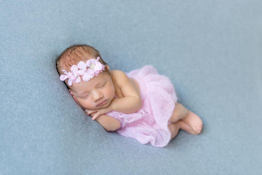 Sweet baby girl sleeping on her tummy, wearing pink little dress, in a flowery hairband