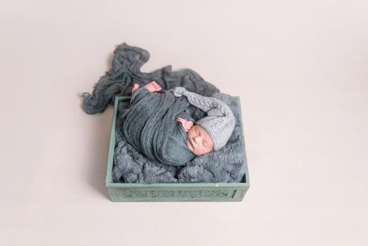Cute newborn covered with huge dark blanket resting in a basket, wearing big hat, topview