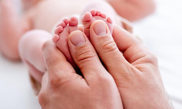 Mother holding tiny newborn baby feet with little fingers closeup. Mom and infant child legs. Concept of matherinity love, care and tenderness