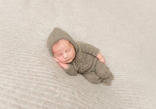 Sweet infant taking a nap in brown knitted clothes, on side, hand under his cheek