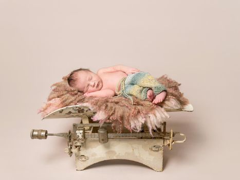 Lovely baby sleeping on old rusty scales, wearing multicolored pants, on soft pillow