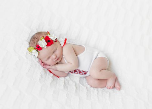 Sweet girl in bright Ukrainian colorful hairband and a white suit sleeps tight on her side