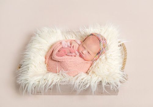 Tiny baby girl in a colorful knitted hat napping sweetly in her child's basket