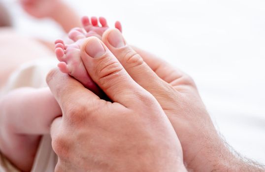 Mother holding tiny newborn baby feet with little fingers in her hands closeup. Mom and infant child legs. Concept of matherinity love, care and tenderness