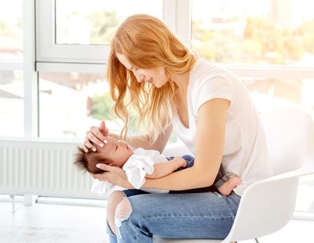 Mother holding her child sitting on chair in light room