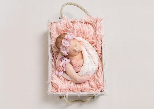 Adorable baby girl wrapped in a white blanket isleeping on a pink soft blanket, topview