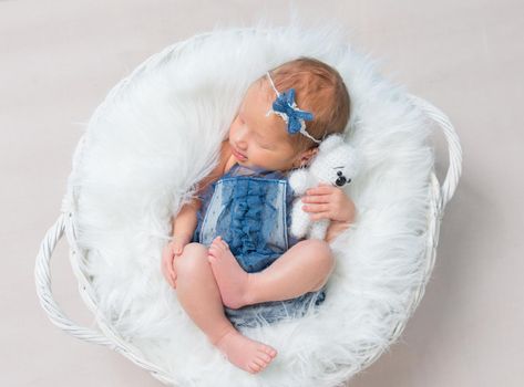 Little baby girl in jeans costume napping in her child's basket with bear toy, topview