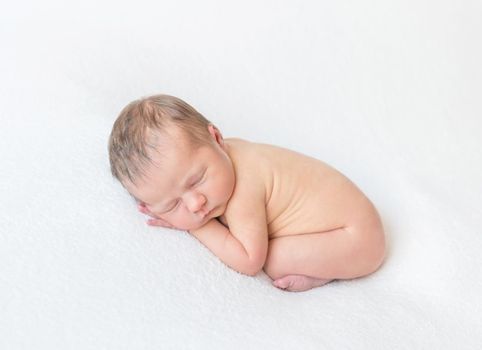 Cute naked baby sleeping on his belly, curled up, laying on white surface