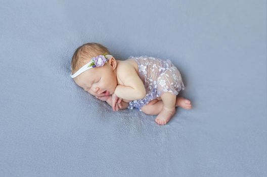 Cute infant sleeping covered with purple veil with flowers on purple soft surface