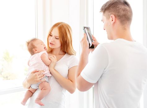 Mother and baby posing for father taking photo indoors