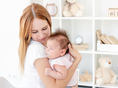 Mother calming baby with soother in light room