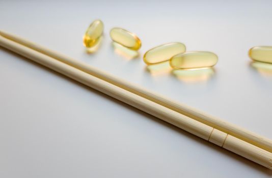 Fish oil capsules with Chinese chopsticks. Omega 3 on a white background. High Resolution Product. Food supplement. Vitamins for a healthy lifestyle. Fatty acid. Metabolism in the body