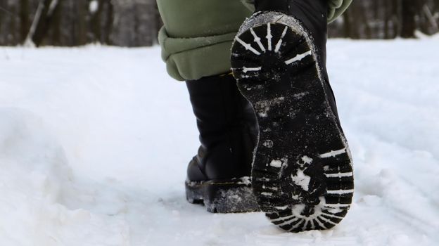 Female legs in black boots, winter walk in the snow. Active woman walking away from the camera in the winter forest. Focus on your legs. Beautiful white winter weather with fresh snowfall