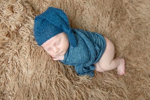 Little kid wrapped in a blue scarf in a hat resting, topview