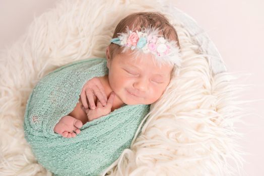Adorable cute baby smiling in her sleep, hairband with flowers, wrapped tightly, closeup