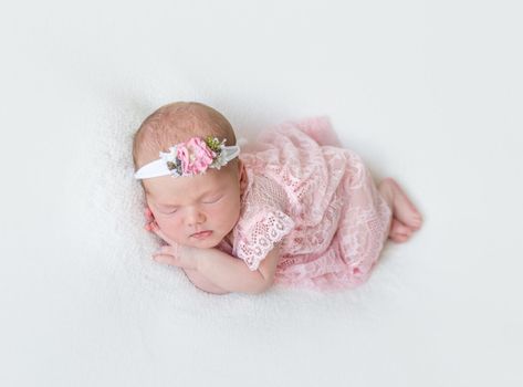 Cute infant with pink flowery hairband dressed in laced costume napping tightly on her side