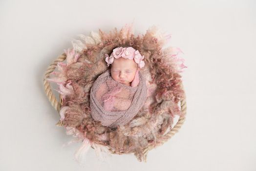 Adorable baby in flowery hairband sleeping on furry pillow, wrapped in scarf, topview