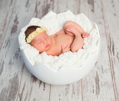 lovely sleeping bare newborn girl with headband with crossed legs in eggshell basket