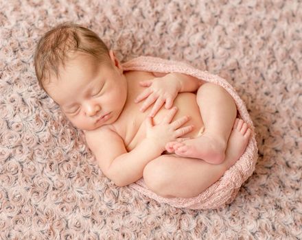 lovely newborn curled up asleep, wrapped in pink diaper on knitted blanket