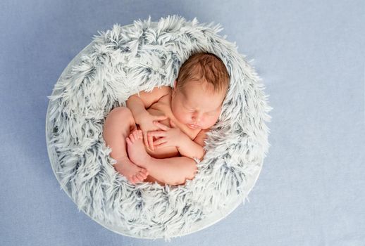 funny little naked newborn baby with crossed legs sleeping in basket, top view