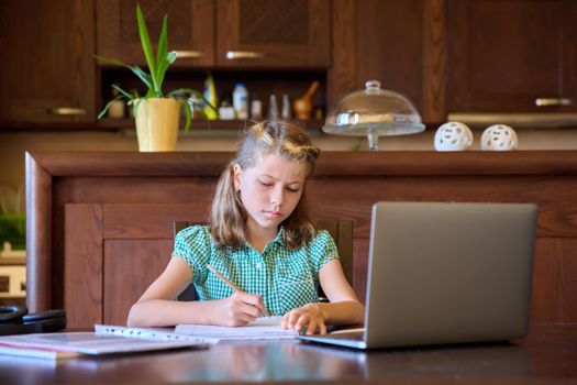 Serious girl child studying at home, with laptop. Focused preteen student writing in a notebook. Remote distance lesson, e-education, study, children, modern school concept