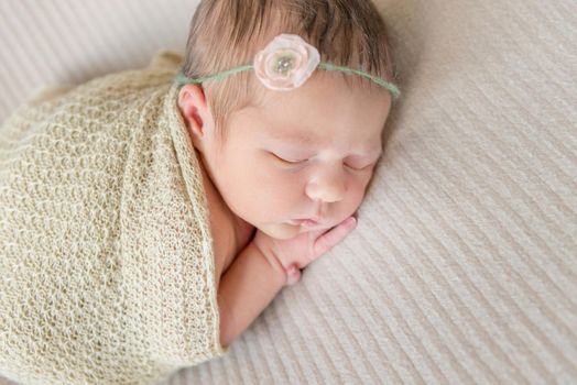 Little baby girl sleeping on her belly, wrapped up with a scarf, in hairband, closeup